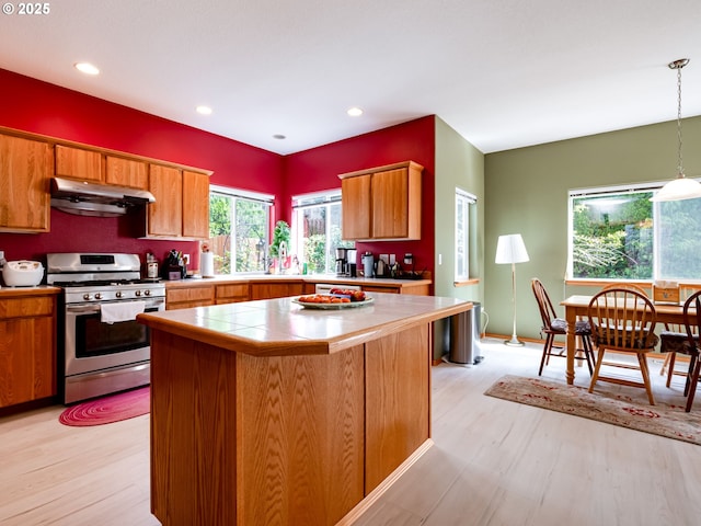 kitchen featuring stainless steel gas stove, light wood-type flooring, a kitchen island, under cabinet range hood, and brown cabinets