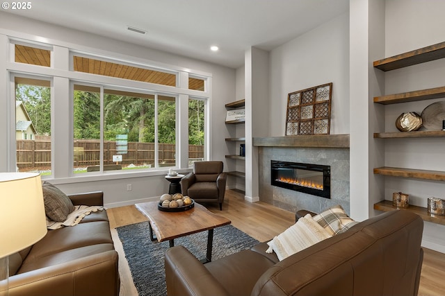 living area with built in features, visible vents, a tile fireplace, and wood finished floors