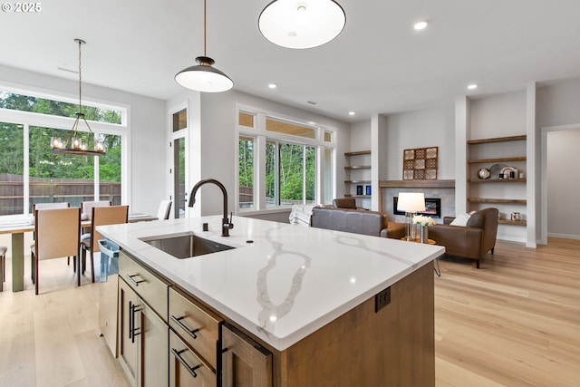 kitchen featuring an island with sink, a sink, a glass covered fireplace, built in features, and light wood-style floors