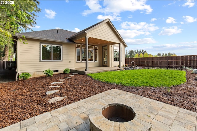 rear view of property with roof with shingles, a fire pit, fence, and a patio