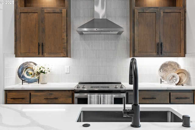 kitchen with dark brown cabinetry, a sink, wall chimney exhaust hood, tasteful backsplash, and stainless steel electric stove