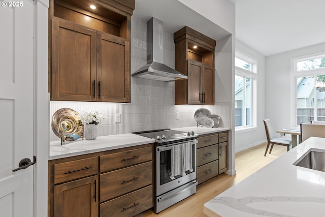 kitchen featuring tasteful backsplash, stainless steel electric range, light wood-type flooring, light stone counters, and wall chimney range hood