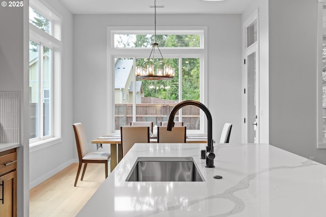 kitchen with light wood finished floors, a wealth of natural light, light stone countertops, and a sink