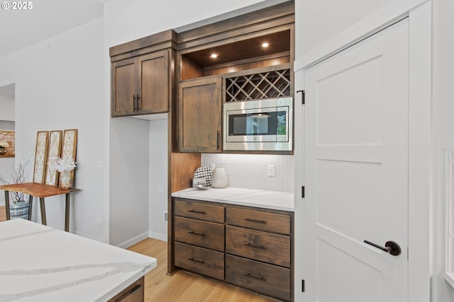 kitchen featuring baseboards, stainless steel microwave, tasteful backsplash, light wood-type flooring, and light stone counters