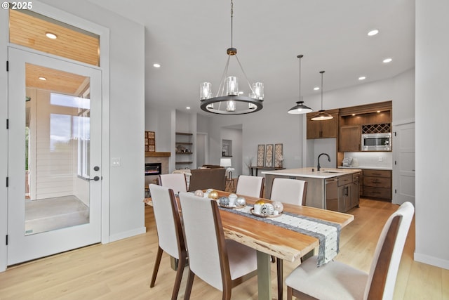 dining room with a glass covered fireplace, recessed lighting, a notable chandelier, and light wood finished floors