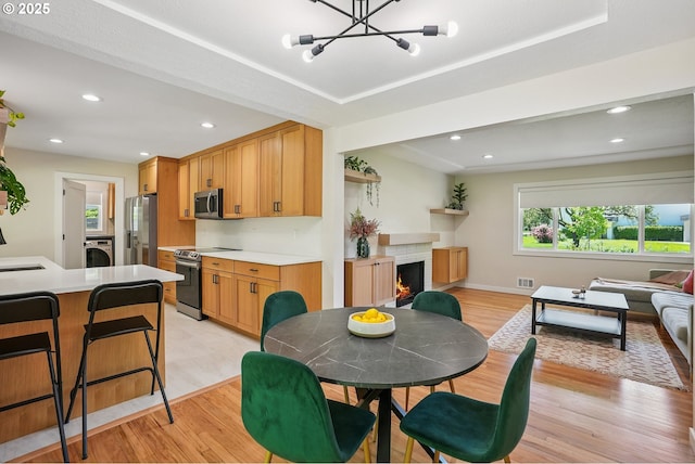 10559 NE Thompson St, Portland, OR 97220 - dining room with light wood-style floors, washer / dryer, recessed lighting, a chandelier, and a warm lit fireplace
