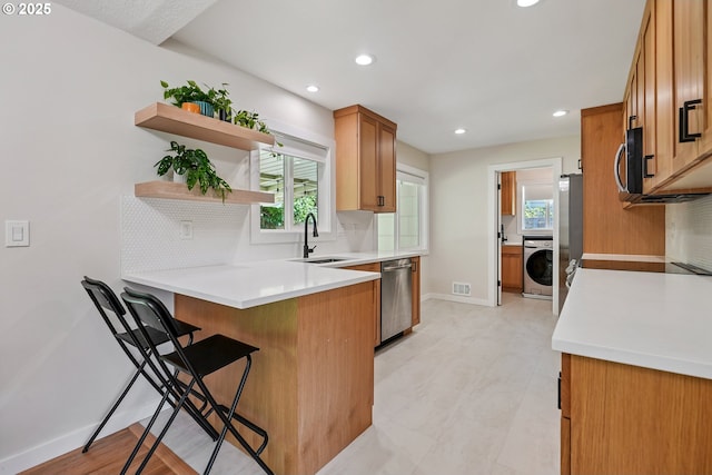 10559 NE Thompson St, Portland, OR 97220 - kitchen featuring washer / dryer, a sink, appliances with stainless steel finishes, decorative backsplash, and a peninsula