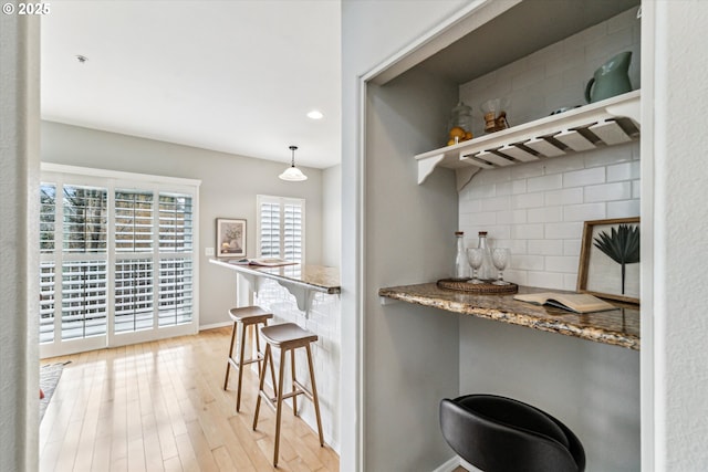 bar with a bar, light wood finished floors, tasteful backsplash, and baseboards