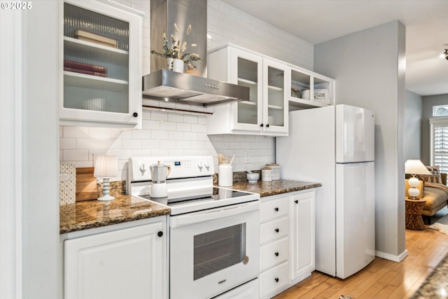 kitchen with white appliances, white cabinetry, light wood-style floors, wall chimney range hood, and tasteful backsplash