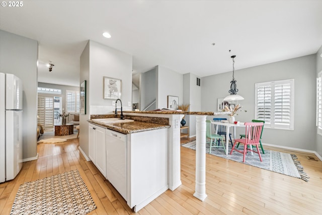 kitchen with white cabinets, a sink, dark stone countertops, light wood-type flooring, and white appliances