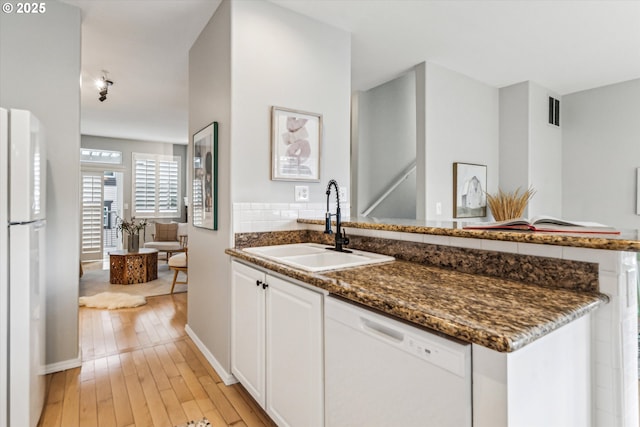 kitchen featuring a peninsula, white appliances, a sink, white cabinetry, and light wood-style floors