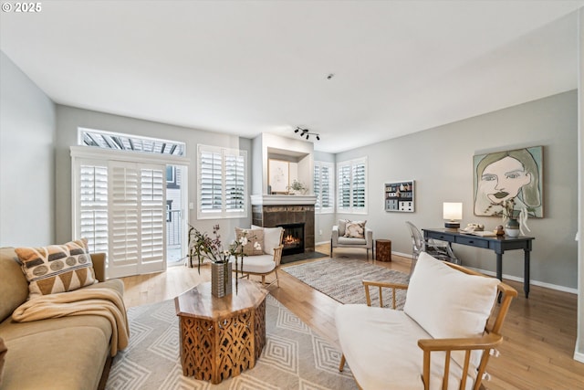 living room featuring a tiled fireplace, baseboards, track lighting, and wood finished floors