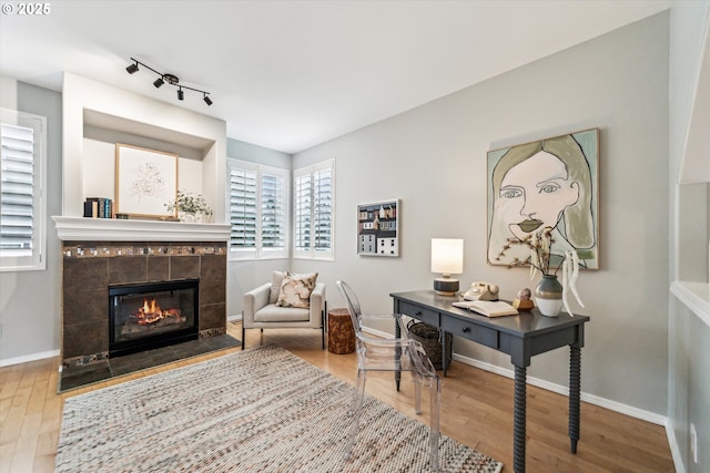 office with rail lighting, a tiled fireplace, baseboards, and wood finished floors