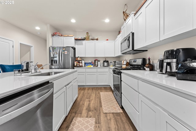 kitchen with appliances with stainless steel finishes, white cabinets, hardwood / wood-style floors, and sink