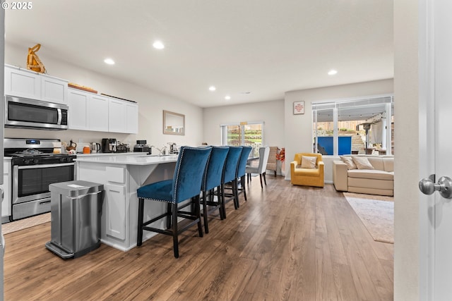 kitchen with stainless steel appliances, white cabinets, a center island, a kitchen bar, and hardwood / wood-style floors