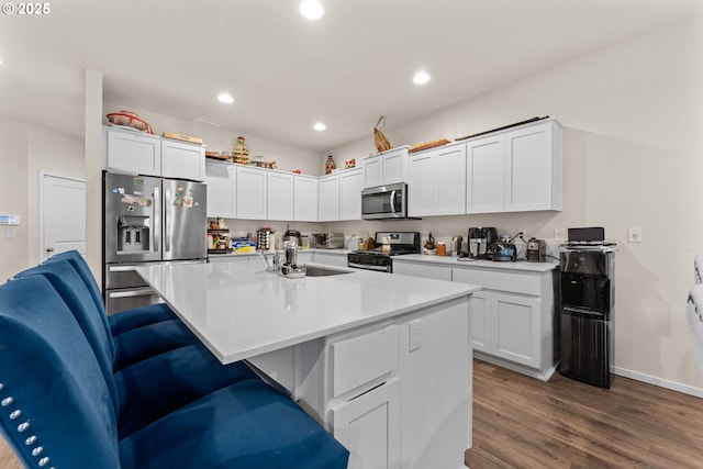 kitchen featuring white cabinetry, a kitchen breakfast bar, dark hardwood / wood-style floors, a center island with sink, and appliances with stainless steel finishes