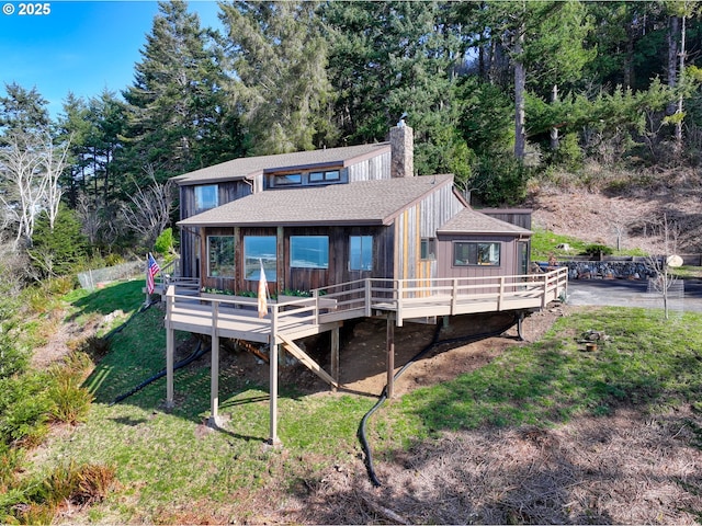 back of property featuring a shingled roof, a yard, a chimney, and a wooden deck