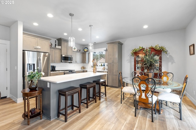 kitchen featuring light wood-type flooring, decorative backsplash, pendant lighting, and appliances with stainless steel finishes