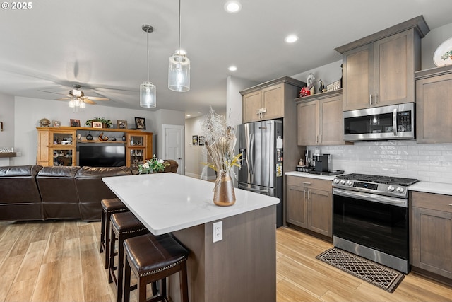 kitchen with pendant lighting, ceiling fan, appliances with stainless steel finishes, a kitchen island, and a breakfast bar area