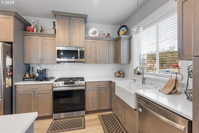 kitchen featuring hanging light fixtures, appliances with stainless steel finishes, sink, light wood-type flooring, and decorative backsplash