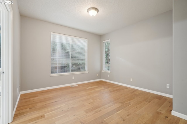 empty room with visible vents, light wood-style flooring, baseboards, and a textured ceiling