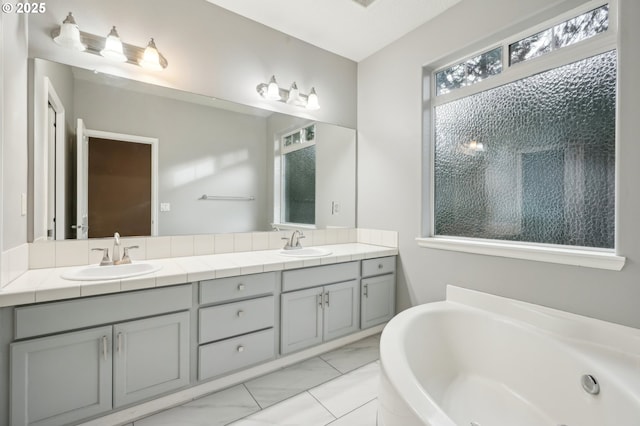 full bathroom with double vanity, marble finish floor, a bathing tub, and a sink