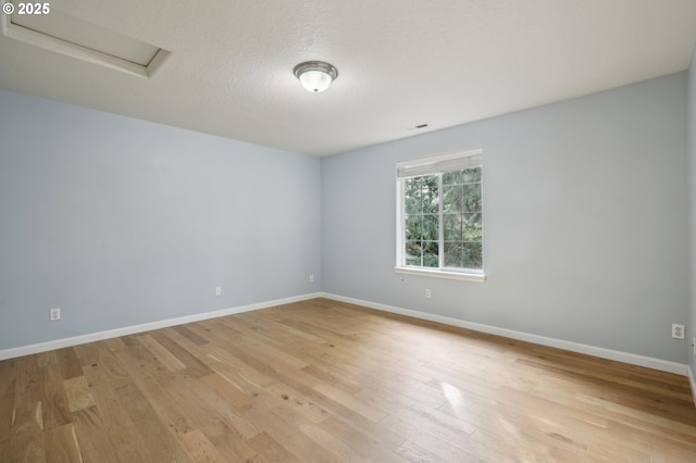 empty room featuring baseboards, a textured ceiling, light wood-style flooring, and attic access