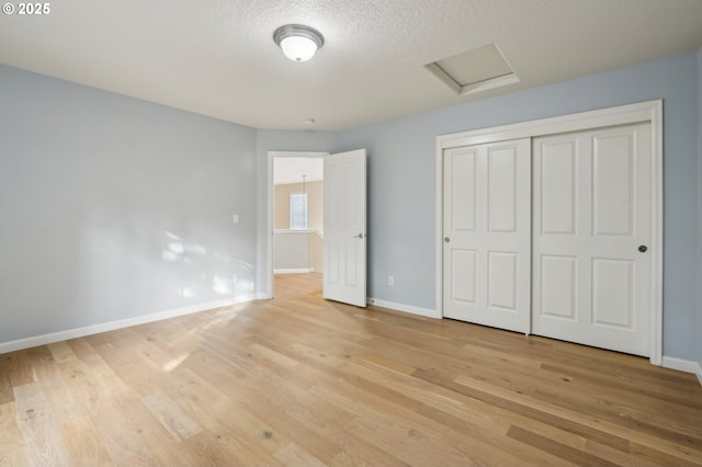 unfurnished bedroom featuring a textured ceiling, baseboards, a closet, light wood-type flooring, and attic access