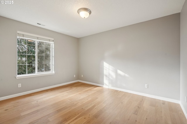 spare room featuring baseboards, a textured ceiling, visible vents, and light wood-style floors