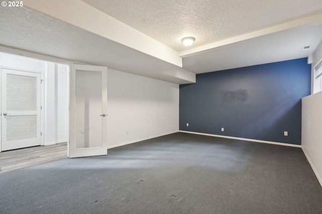 below grade area with a textured ceiling, carpet, visible vents, and baseboards