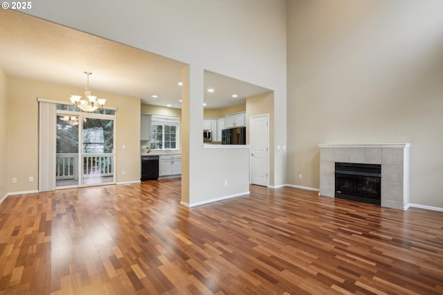 unfurnished living room with a tile fireplace, wood-type flooring, a notable chandelier, and a towering ceiling