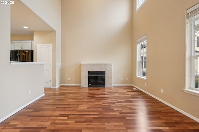 unfurnished living room featuring a towering ceiling, a tiled fireplace, baseboards, and wood finished floors