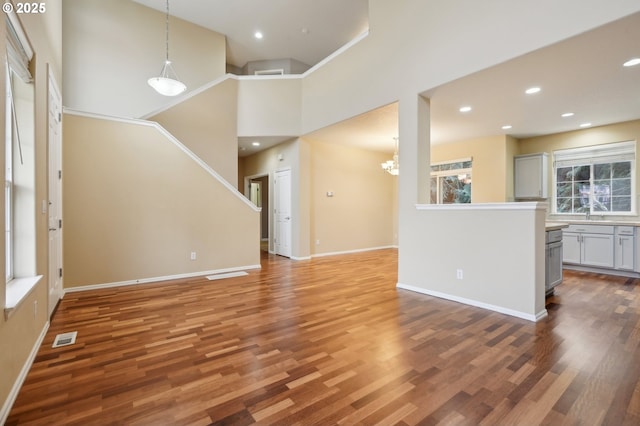 unfurnished living room with recessed lighting, visible vents, a high ceiling, wood finished floors, and baseboards