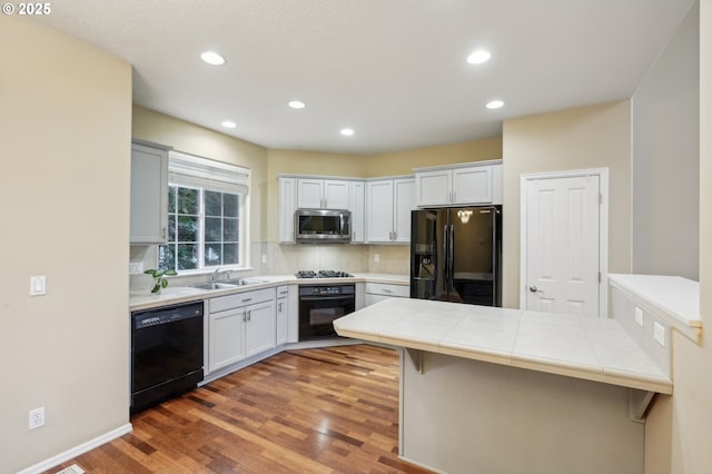 kitchen featuring tile countertops, tasteful backsplash, a sink, wood finished floors, and black appliances