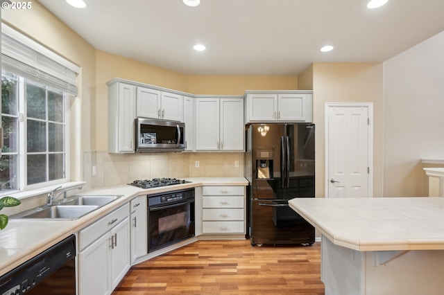 kitchen with light wood finished floors, decorative backsplash, black appliances, a sink, and recessed lighting