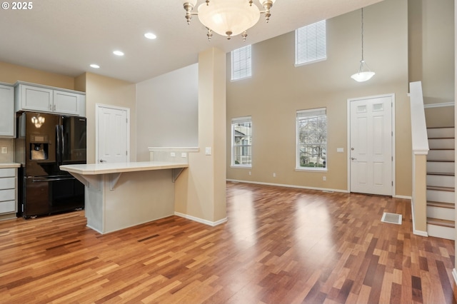 kitchen with white cabinetry, hanging light fixtures, a kitchen bar, black fridge, and light wood-type flooring