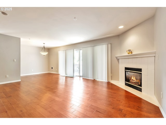 unfurnished living room featuring a tiled fireplace, recessed lighting, baseboards, and wood finished floors