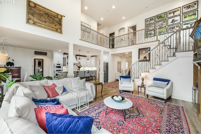 living room featuring baseboards, light wood-style floors, a towering ceiling, stairway, and ornate columns