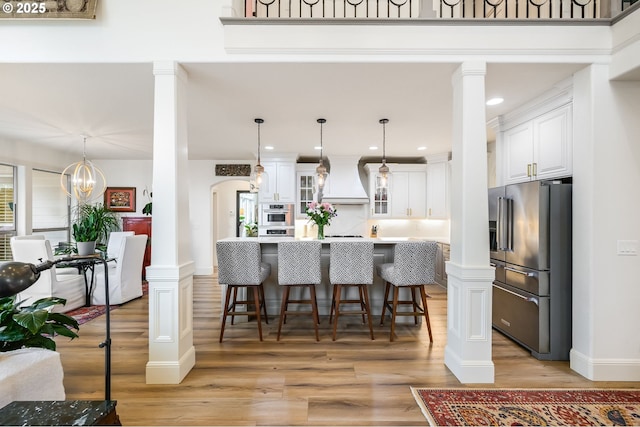 kitchen with arched walkways, custom range hood, appliances with stainless steel finishes, white cabinetry, and ornate columns