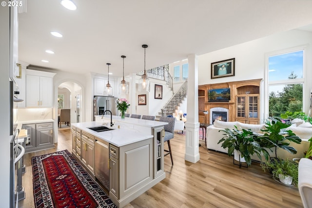 kitchen featuring arched walkways, a sink, appliances with stainless steel finishes, light wood finished floors, and a glass covered fireplace