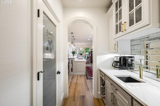 bar featuring arched walkways, a sink, light wood-style flooring, and decorative backsplash