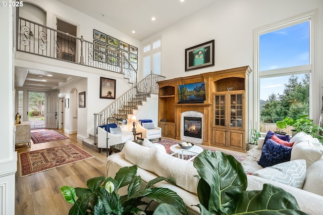 living area with a healthy amount of sunlight, a high ceiling, wood finished floors, and a glass covered fireplace