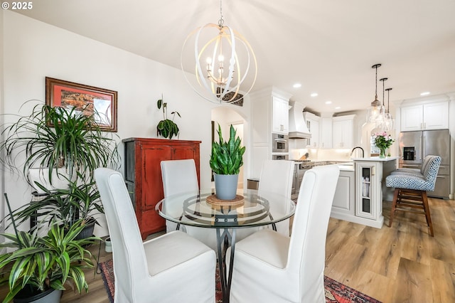 dining area featuring arched walkways, a notable chandelier, light wood-style flooring, and recessed lighting