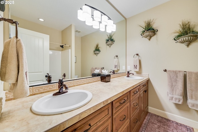 bathroom with walk in shower, a sink, baseboards, and double vanity