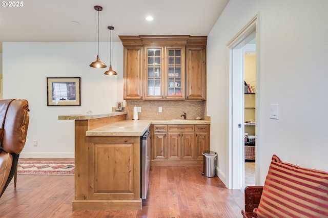 kitchen with a peninsula, wood finished floors, brown cabinets, tasteful backsplash, and glass insert cabinets