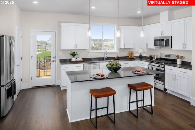 kitchen featuring dark countertops, appliances with stainless steel finishes, a breakfast bar, dark wood-type flooring, and a sink