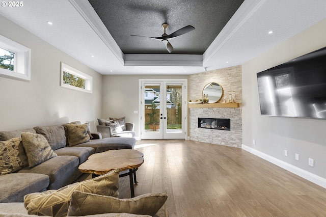 living room featuring a raised ceiling, wood-type flooring, a stone fireplace, a textured ceiling, and french doors