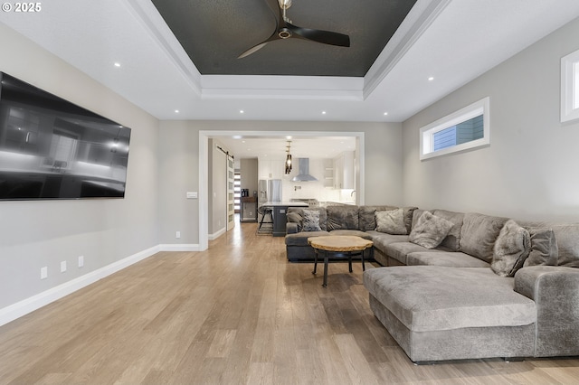 living room with a raised ceiling, ceiling fan, and light hardwood / wood-style flooring