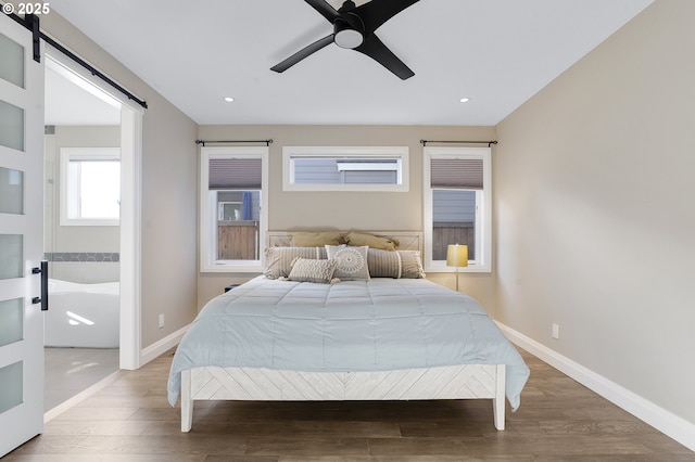 bedroom with ceiling fan, a barn door, and hardwood / wood-style flooring