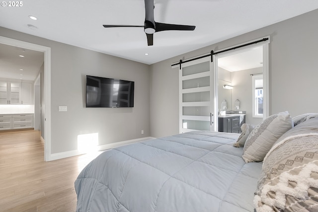 bedroom featuring ceiling fan, a barn door, connected bathroom, and light hardwood / wood-style floors